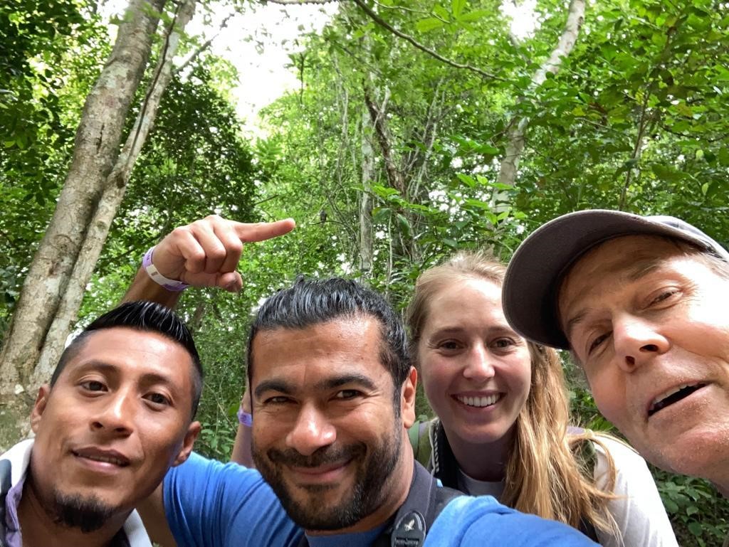 Tikal Expedition Team - Esdras (a biologist from Tikal), Julio, Hana, and Russell. Julio is pointing to a tiny Barred Forest Falcon perched high above in the tree behind the team.