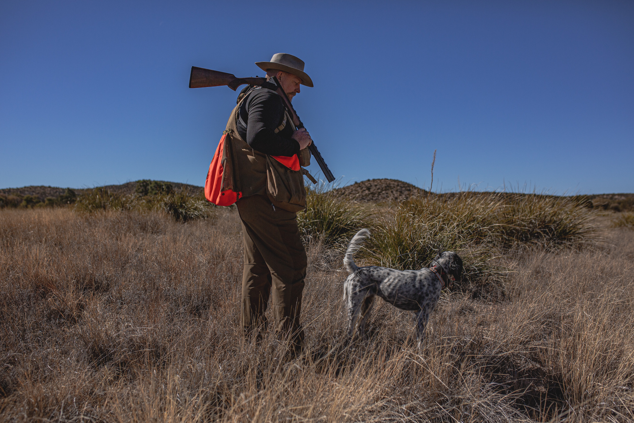 Peregrine Fund CEO Chris Parish, dressed in hunting clothes, walks through a field with his hunting dog and shotgun draped over his shoulder.