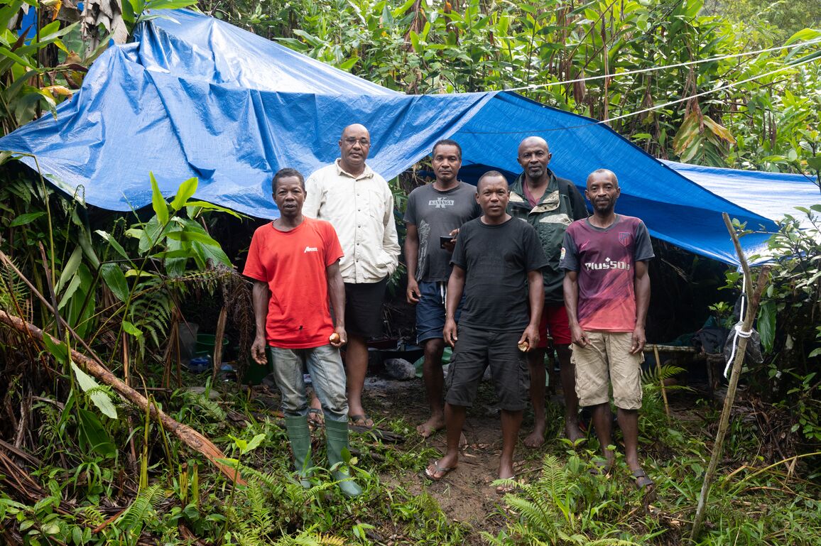 Six men in a jungle stand in front of a tent